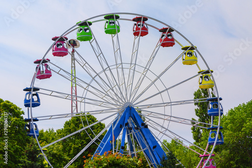 Ferris wheel without people , among green on the blue sky background