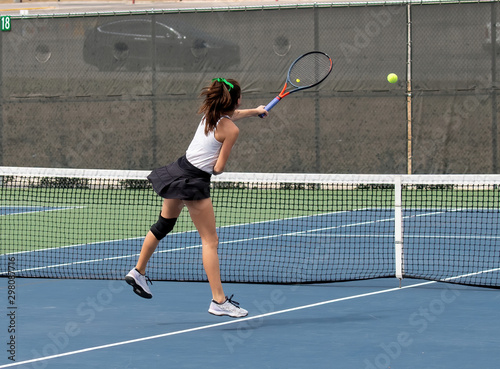Young girl serving and volleying the ball during a tennis match © Joe