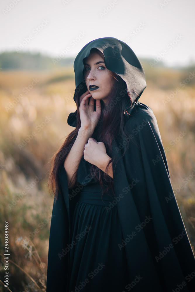 A girl in a black dress, a cloak with a hood. It stands in a high