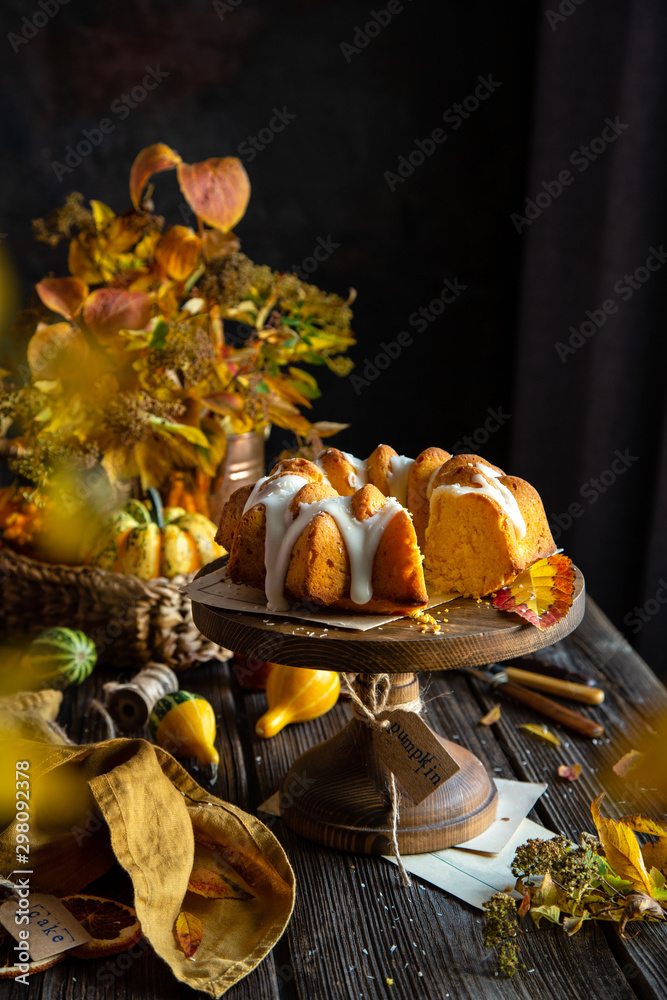 homemade tasty baked bundt pumpkin cake with glaze on top on wooden cake stand