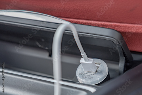 Close-up, isolated view of a automotive cigarette lighter being used as a USB phone charger. The background shows some of the red leather of this german car.