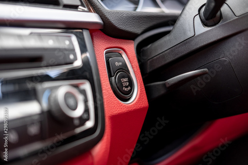 Close-up, isolated image of an engine Start Stop button seen on the dashboard of a german manufactured sports car, also showing its part red leather.