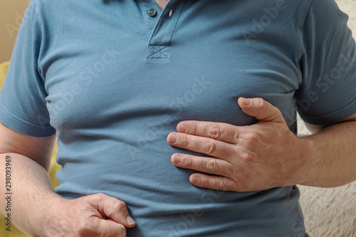 A man in a blue T-shirt holds his hands in his heart. Heart health problems