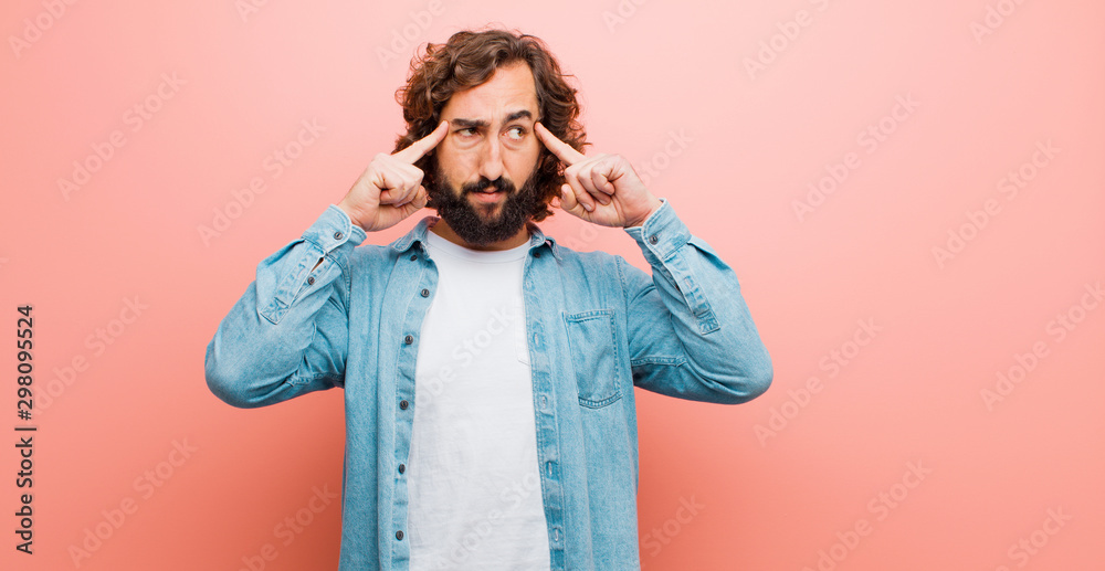 young bearded crazy man feeling confused or doubting, concentrating on an idea, thinking hard, looking to copy space on side against flat color wall - obrazy, fototapety, plakaty 