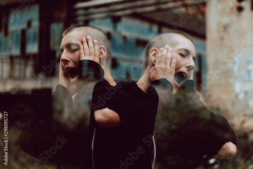 Reflected crazy female with short hair keeping hands near face and shouting loudly while standing on blurred background of grungy street photo