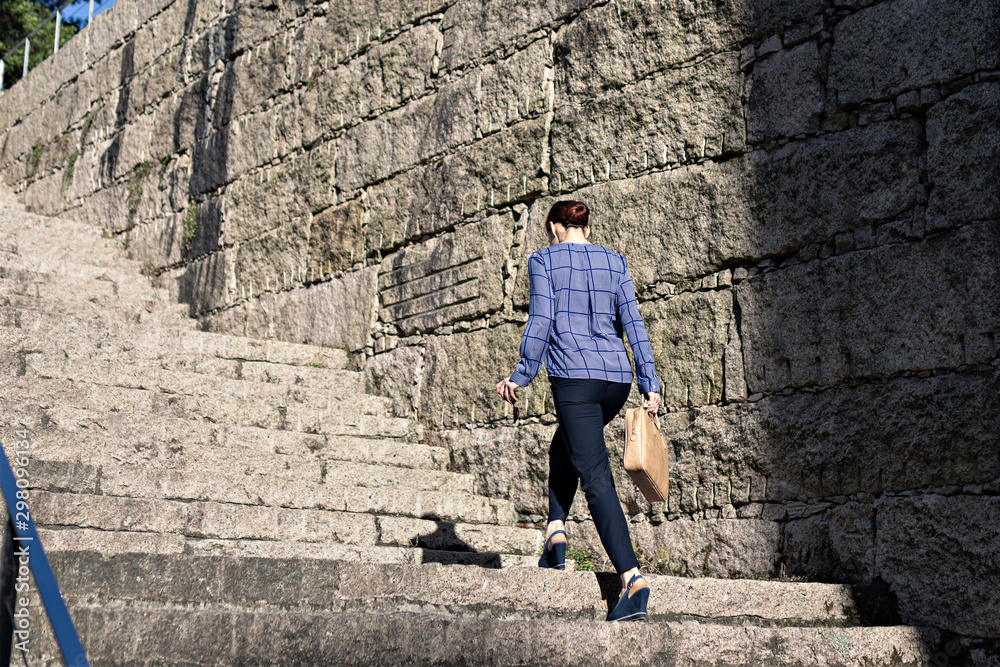 Low angle of elegant entrepreneur with stylish briefcase walking up rough steps on sunny day on city street Low angle of elegant entrepreneur with stylish briefcase walking up rough steps on sunny day on city street