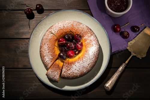 Round cherry cake in plate on wooden table. Dark food photo