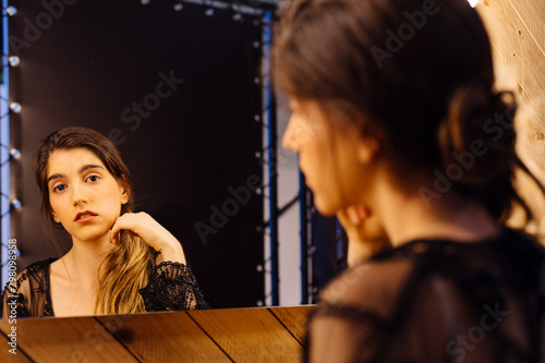 Back view of sad attractive woman in lace peignoir sitting in dressing room looking in mirror and making hair