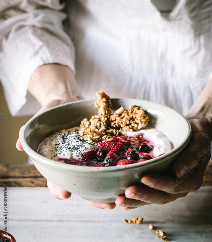 Crop person holding bowl with delicious crispy granola served with fresh berries yogurt and chia seeds