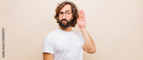 фотографія young bearded crazy man looking serious and curious, listening, trying to hear a