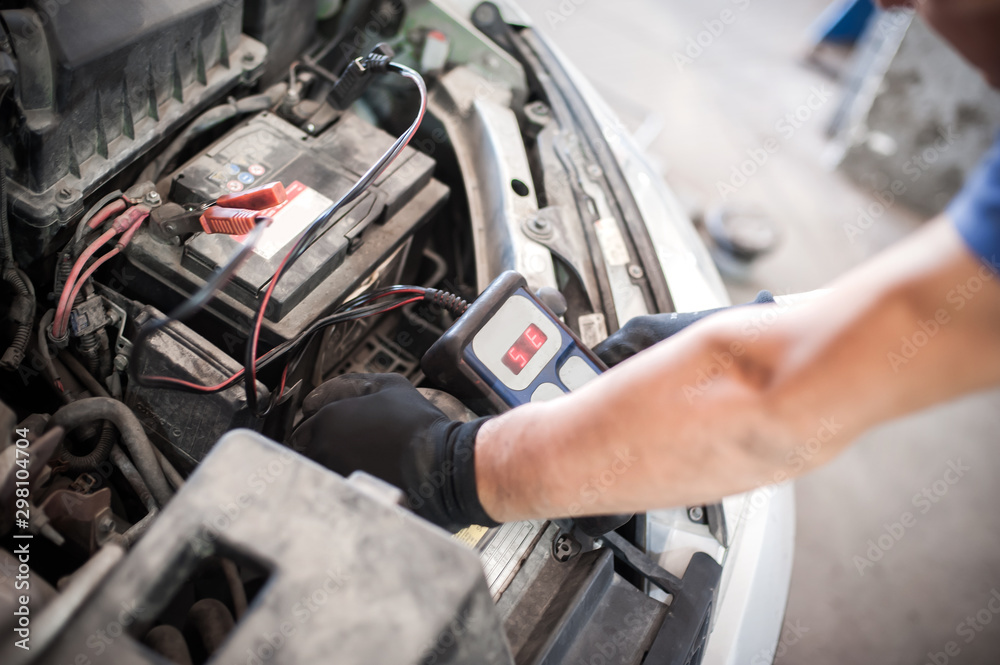 Fototapeta premium Car mechanic checking and testing automotive accumulator with battery tester