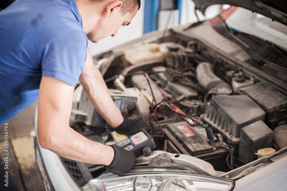 Car mechanic checking and testing automotive accumulator with battery tester Car mechanic checking and testing automotive accumulator with battery tester
