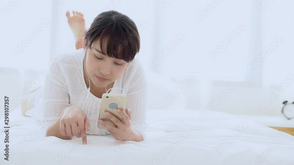 Beautiful portrait young asian woman lying happy earphone listening music with relax and enjoy in the bedroom, girl fun headphone with playing song smart mobile phone, lifestyle concept. Beautiful portrait young asian woman lying happy earphone listening music with relax and enjoy in the bedroom, girl fun headphone with playing song smart mobile phone, lifestyle concept.