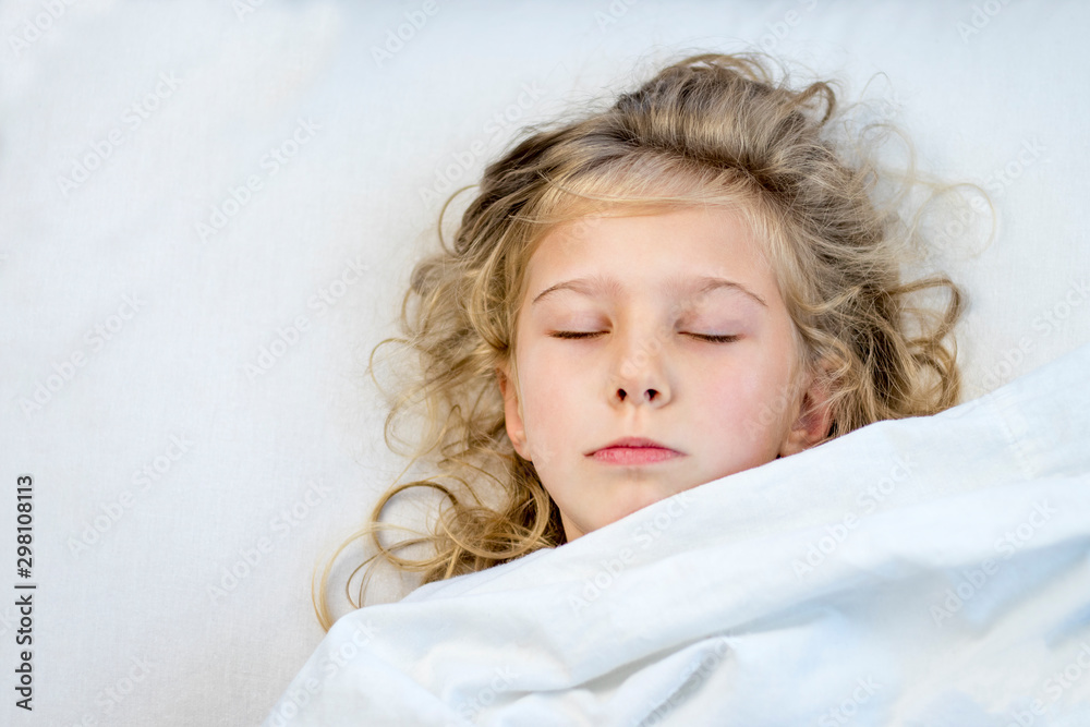 a girl with blond hair she lies in bed under a blanket. she fell asleep. a girl with blond hair she lies in bed under a blanket. she fell asleep.