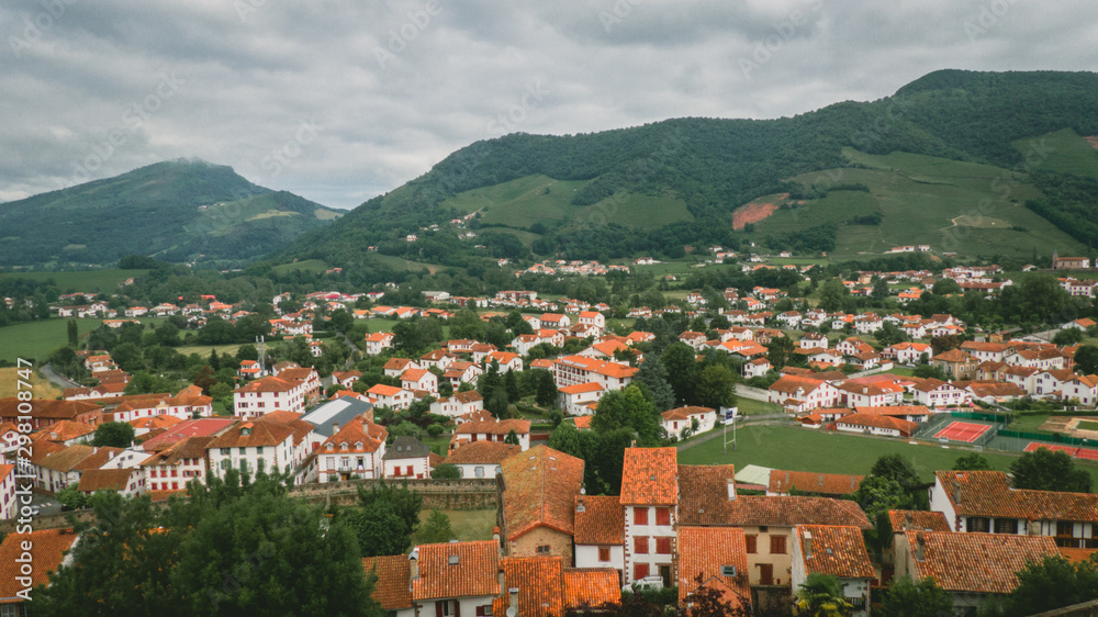 Mountain village with orange roofs and mountains in the background in a cloudy day. (panoramic)