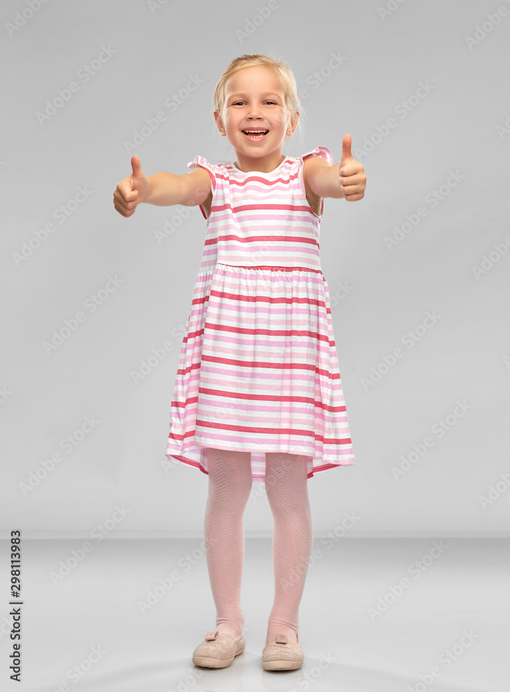 childhood and people concept - beautiful smiling little girl in striped dress showing thumbs up over grey background childhood and people concept - beautiful smiling little girl in striped dress showing thumbs up over grey background