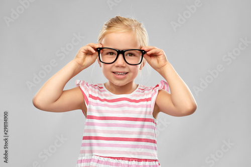 education, school and vision concept - smiling cute little girl in black glasses over grey background