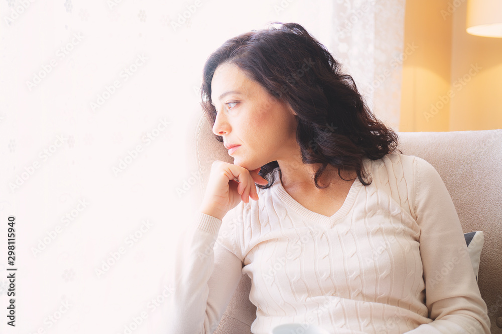 Woman sitting in a comfortable chair drinking coffee and looking through window Woman sitting in a comfortable chair drinking coffee and looking through window