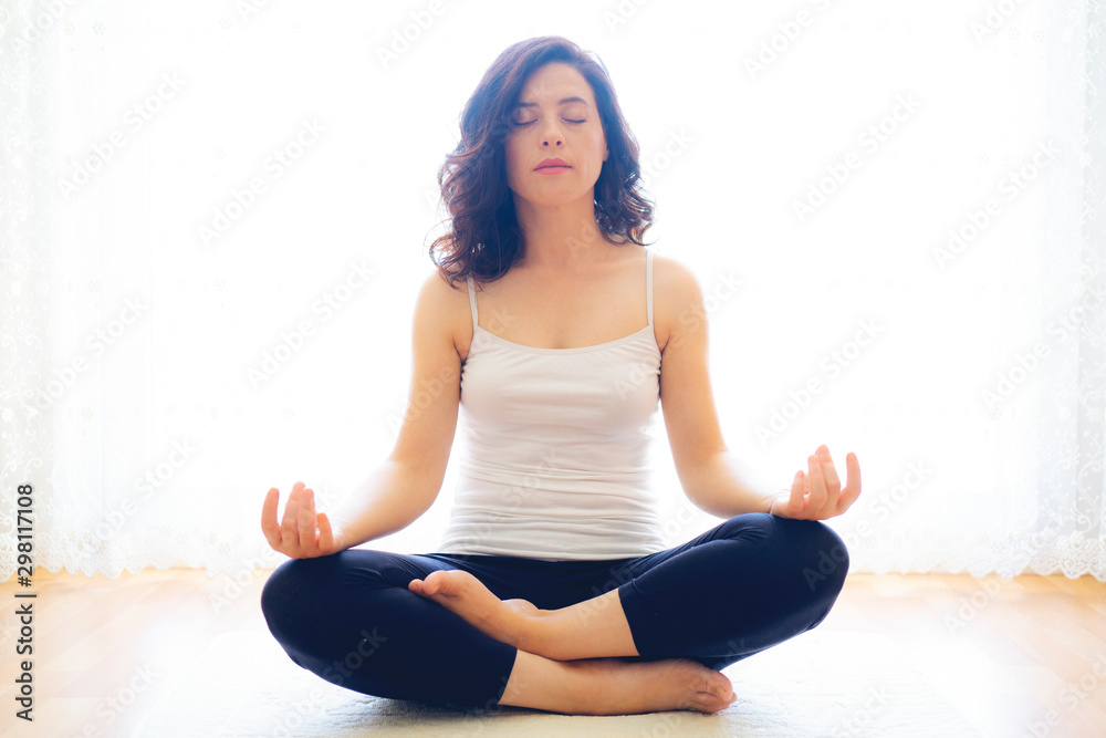 Yoga at home. Keep calm. Attractive young woman sitting on lotus position on floor with eyes closed.