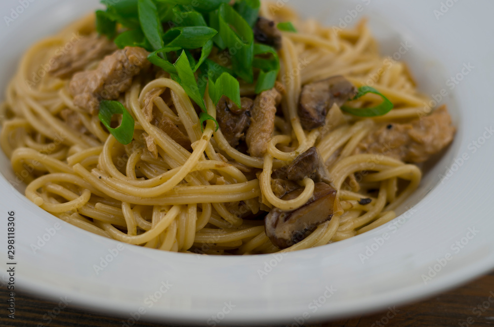 Creamy spaghetti with chicken and mixed mushrooms. Sprinkled with spring onions cut into rings. Freshly prepared and served as a healthy and fast meal of Italian cuisine.