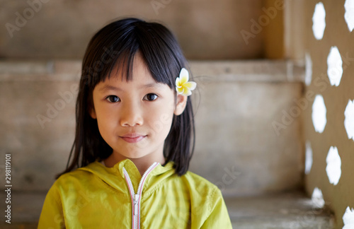 Cute Asian little girl wearing plumeria flowers in front of quaint windows. Travel in Hanoi