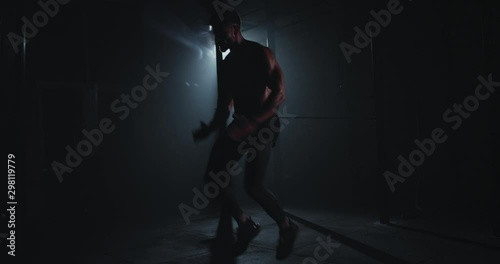 In a dark side gym athletic guy doing intense his workout exercises hard in front of the camera