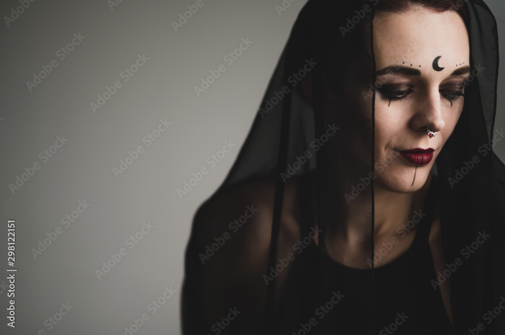 Redhead woman with a black veil on her head in a dark studio. A girl with an earring in her nose smiles slyly. Witch Makeup. Halloween costume. Redhead woman with a black veil on her head in a dark studio. A girl with an earring in her nose smiles slyly. Witch Makeup. Halloween costume.