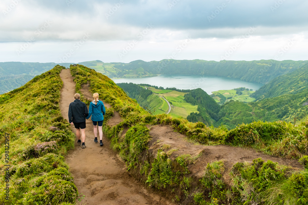 A young couple holding hands while walking towards the Grota do Inferno viewpoint at Sete Cidades on Sao Miguel Island, Azores. The adults are walking away from the camera and looking at the lake view