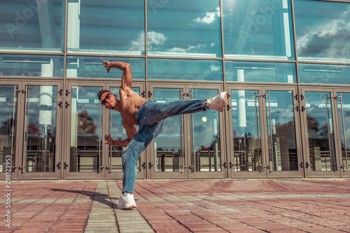 Male athlete, jumping dancing glass window background, summer city, hip hop style, break dancer. Free space motivation text. Active youth lifestyle, fashionable hipster street dancer. Jeans sunglasses