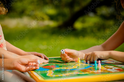 Family playing a board game, one kid is on the move and capturing the piece of another player.Games in Kindergarden.Board game and kids leisure concept. Kids holding red people figure in hand. blue