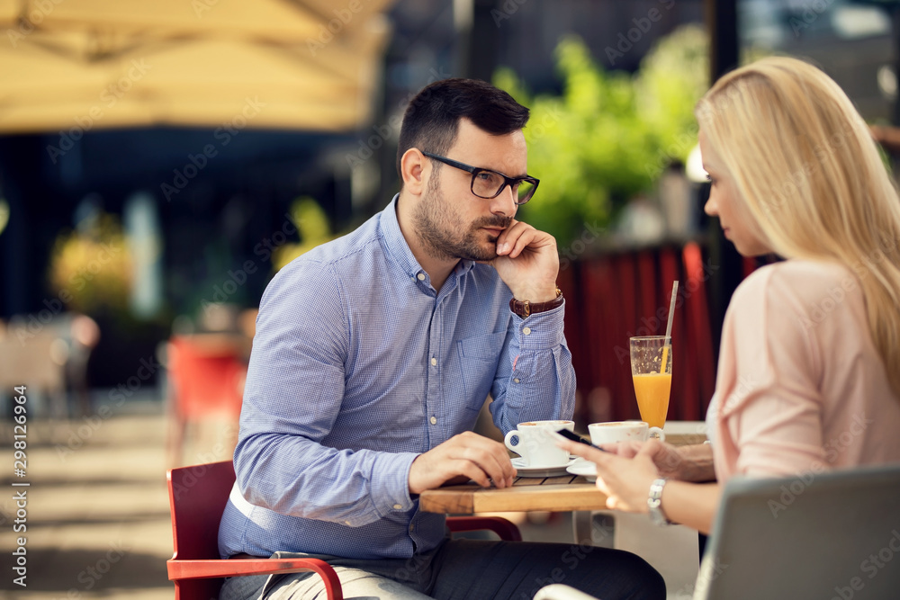 Displeased man looking at his girlfriend who is text messaging on mobile phone in a cafe. Displeased man looking at his girlfriend who is text messaging on mobile phone in a cafe.