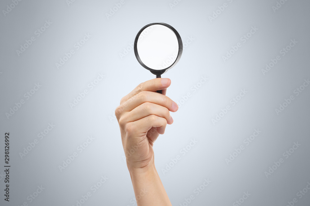 Hand holding a magnifying glass on gray background Hand holding a magnifying glass on gray background