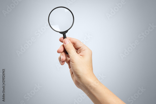 Hand holding a magnifying glass on gray background