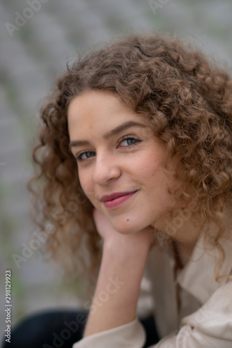 Close up of cheerful young woman with curly hair looking and smiling at the camera