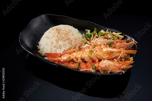 Steam rice and large prawns with sauce on a black plate on a dark background