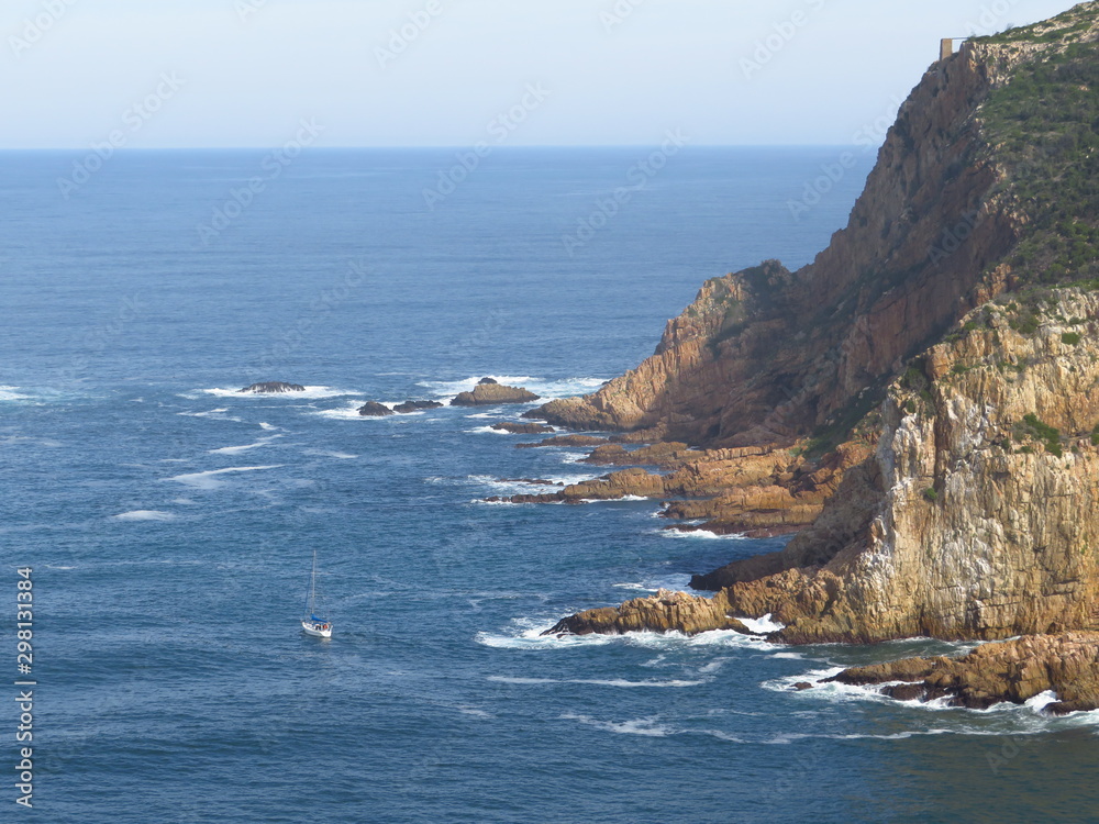 A small yacht rounds the West Heads of Knysna, South Africa.