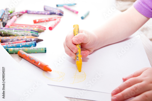 child draws the sun in crayons on paper