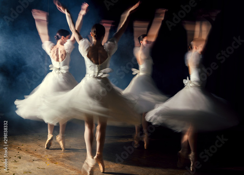 Ballerinas in dresses whirling on scene in darkness in fog
