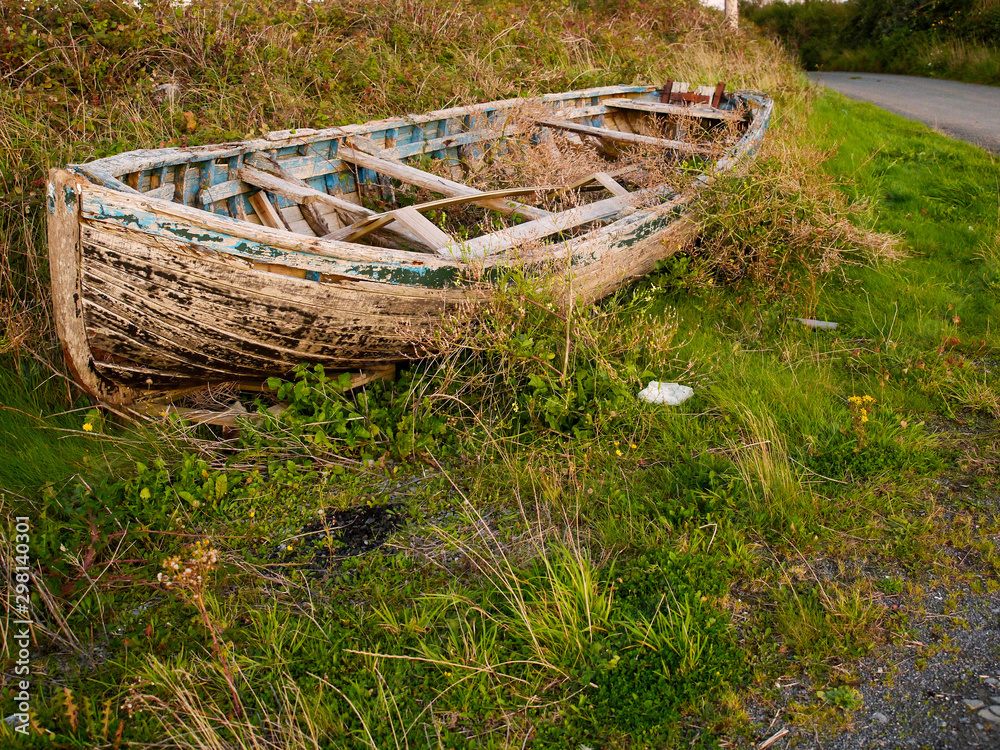 Old rustic wooden fishing boat ashore in the grass, damaged beyond repair Old rustic wooden fishing boat ashore in the grass, damaged beyond repair