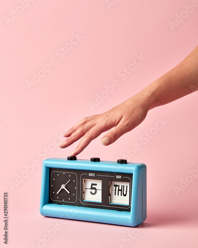 Woman's hand turns off the button on retro flip clock with calendar day thuesday, date 5, on a background color of the year 2019 Living Coral .
