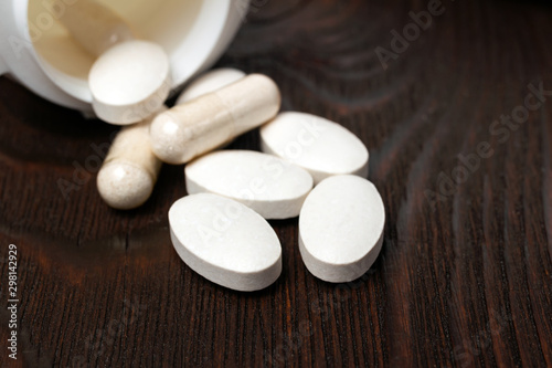 White medical supplement pills and capsules on wooden background, macro image