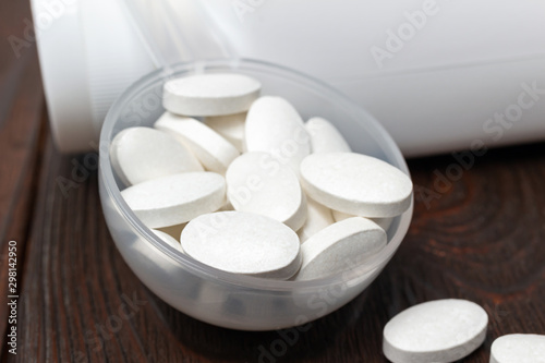 White medical supplement pills in the plastic spoon on wooden background, macro image