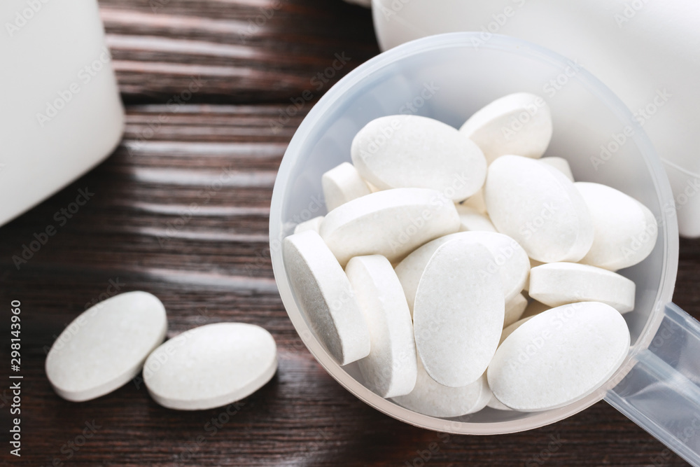 White medical supplement pills in the plastic spoon on wooden background, macro image