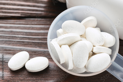 White medical supplement pills in the plastic spoon on wooden background, macro image