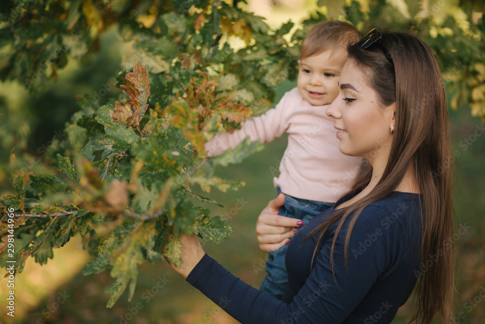 Obraz premium Portrait of beautiful family in the park. Mom and daughter togehter in autumn. Beautiful ten month baby on mother's hands