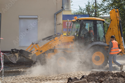 Orange excavator on wheels works in the city