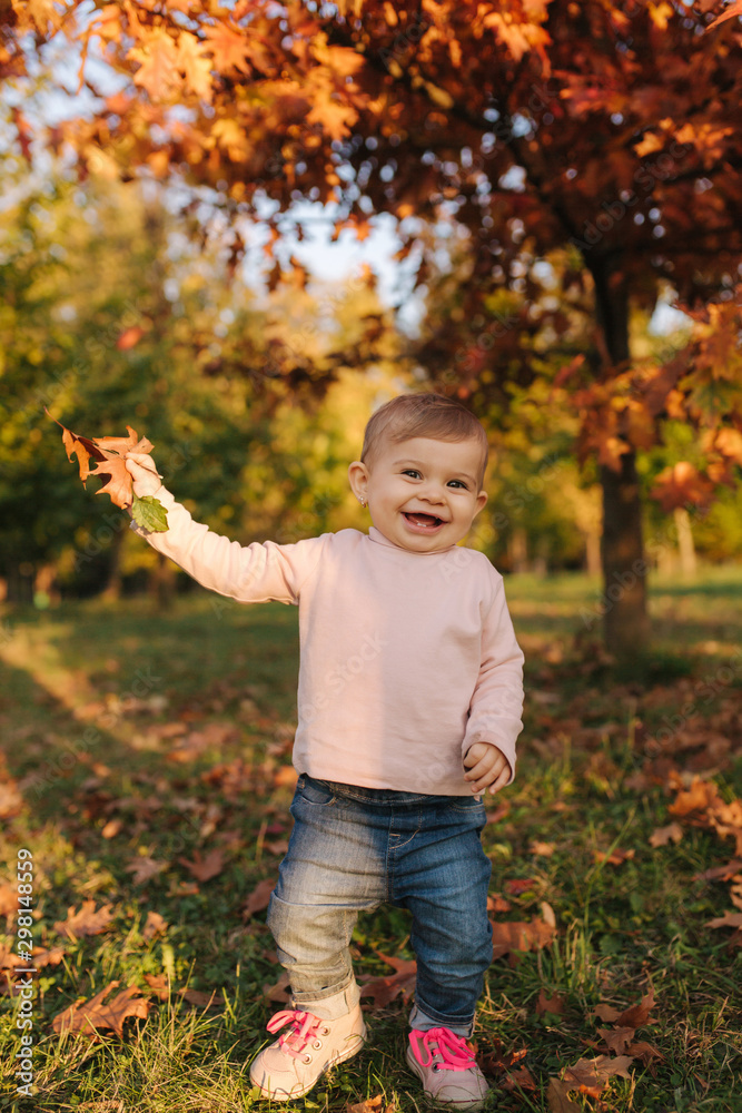 Beautiful little girl play with red leaves near the tree in autumn. Happy ten month baby walking in the park Beautiful little girl play with red leaves near the tree in autumn. Happy ten month baby walking in the park