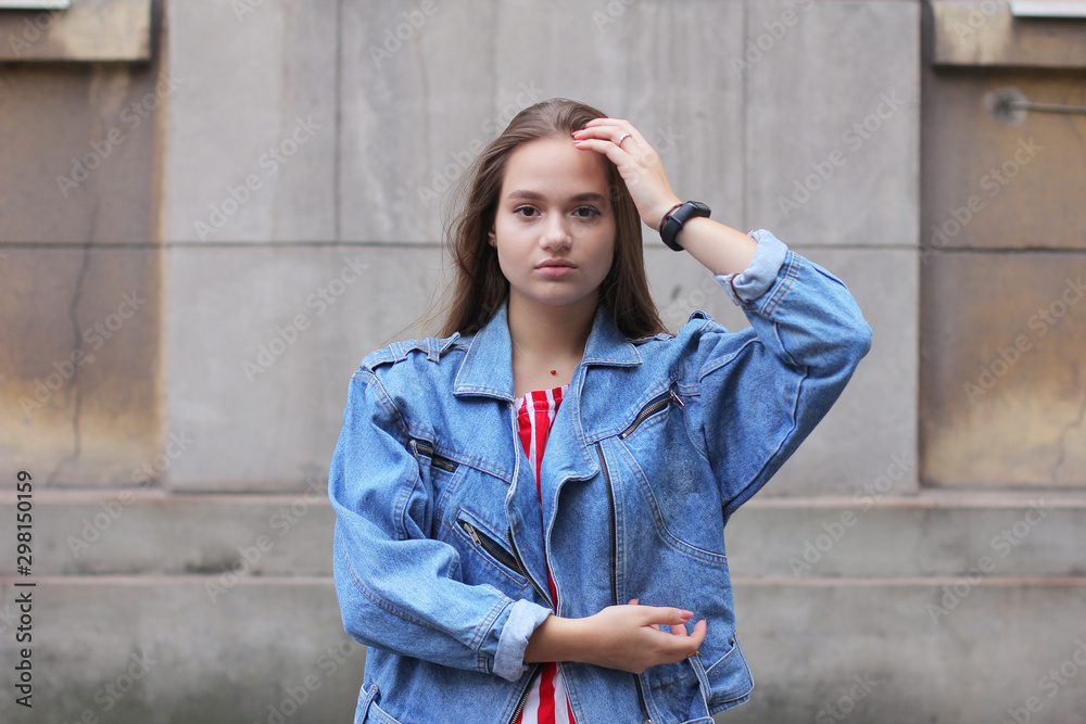 Beautiful young girl in a denim jacket and a bright striped skirt
