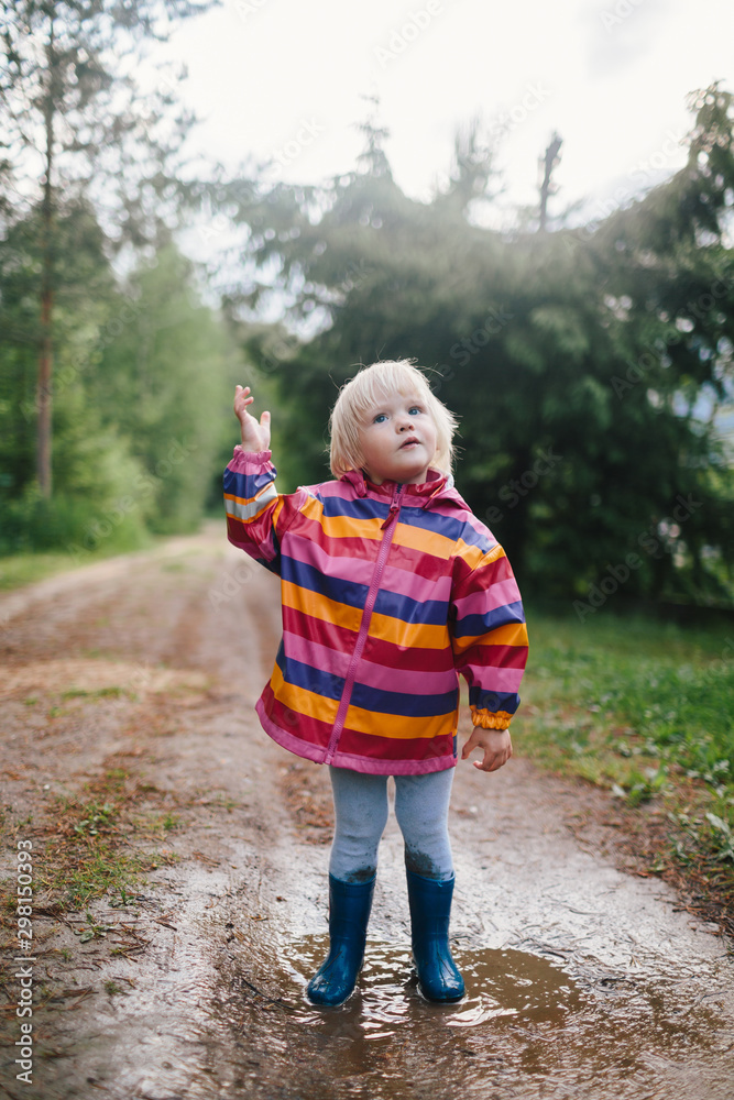 Little kid dressed in multicolor raincoat on the forest path Little kid dressed in multicolor raincoat on the forest path