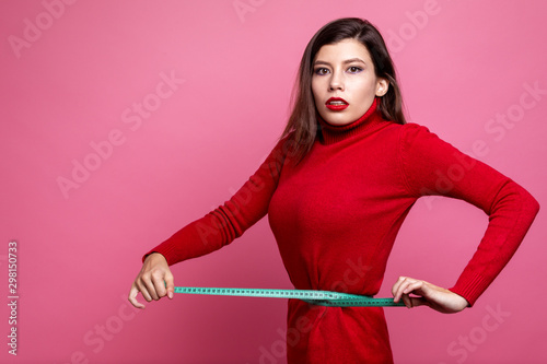 a girl in a red sweater and red pants measures her waist with a centimeter tape measure. the girl tries to match her clothing size